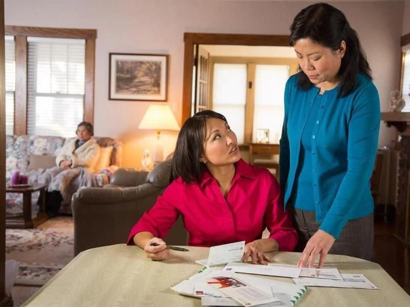 two ladies going over long term care policy with senior sitting on the couch in the background