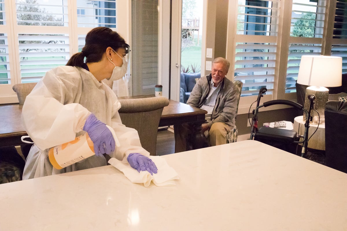 Caregiver in PPE performing Preventative Care while aging adult looks on.