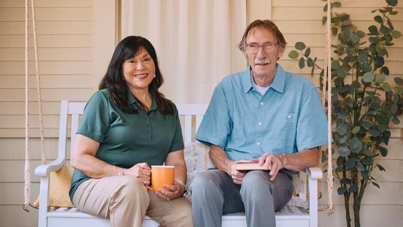 A confident Home Instead caregiver sits with client, smiling warmly, symbolizing professionalism.