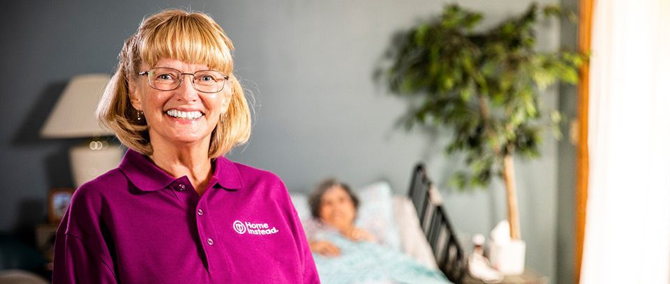 caregiver stands smiling in front of senior woman in bed