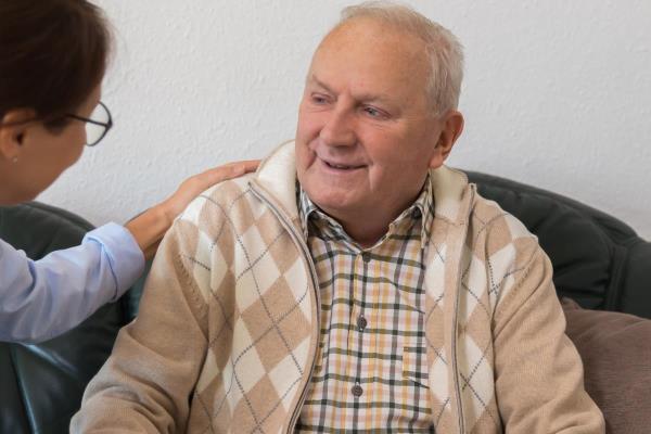 A caregiver compassionately listens to an older man, representing the kind of patience and empathy that help with communicating with clients who have dementia.