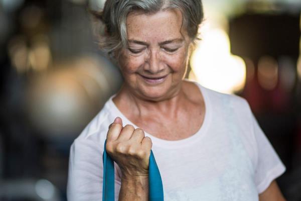 An older woman uses a resistance band to exercise, representing how staying active can help older adults keep their blood pressure in a healthy range.