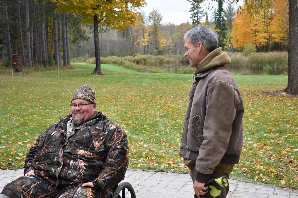 2 men in camouflage next to a field with a lake off in the distance