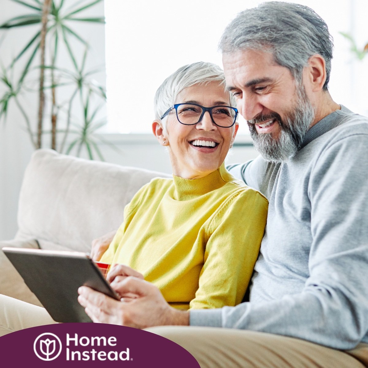 A senior couple smiles while looking at a laptop, showing how online resources can help family caregivers.