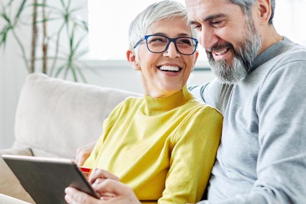 A senior couple smiles while looking at a laptop, showing how online resources can help family caregivers.