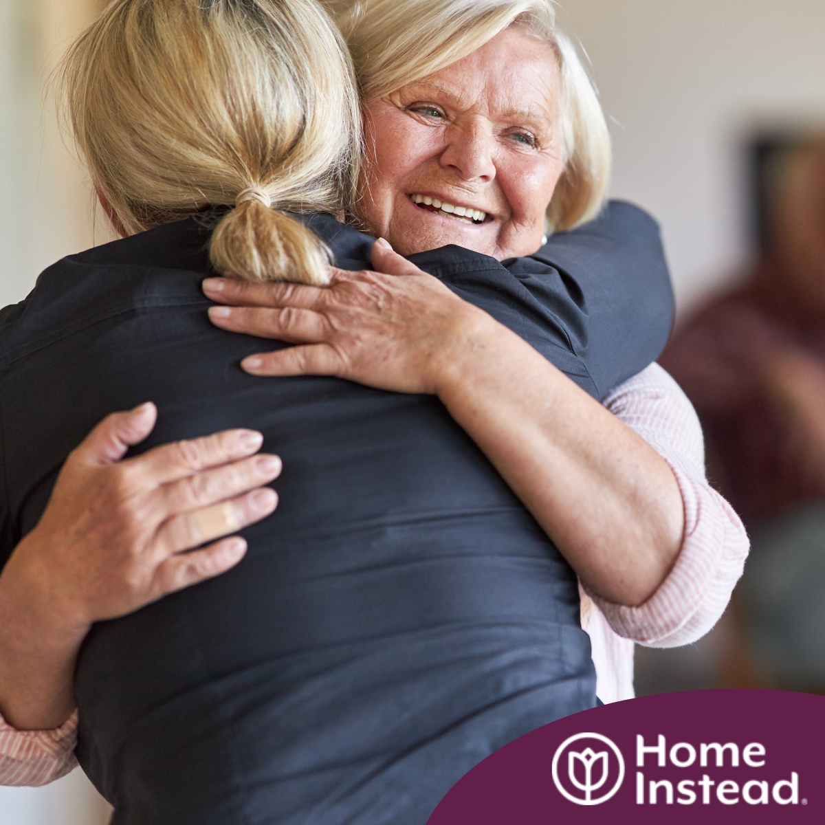 An older woman smiles as a younger woman visits her and hugs her, showing the effect that acts of kindness can have on senior loved ones.