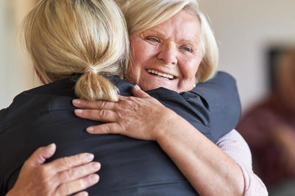 An older woman smiles as a younger woman visits her and hugs her, showing the effect that acts of kindness can have on senior loved ones.