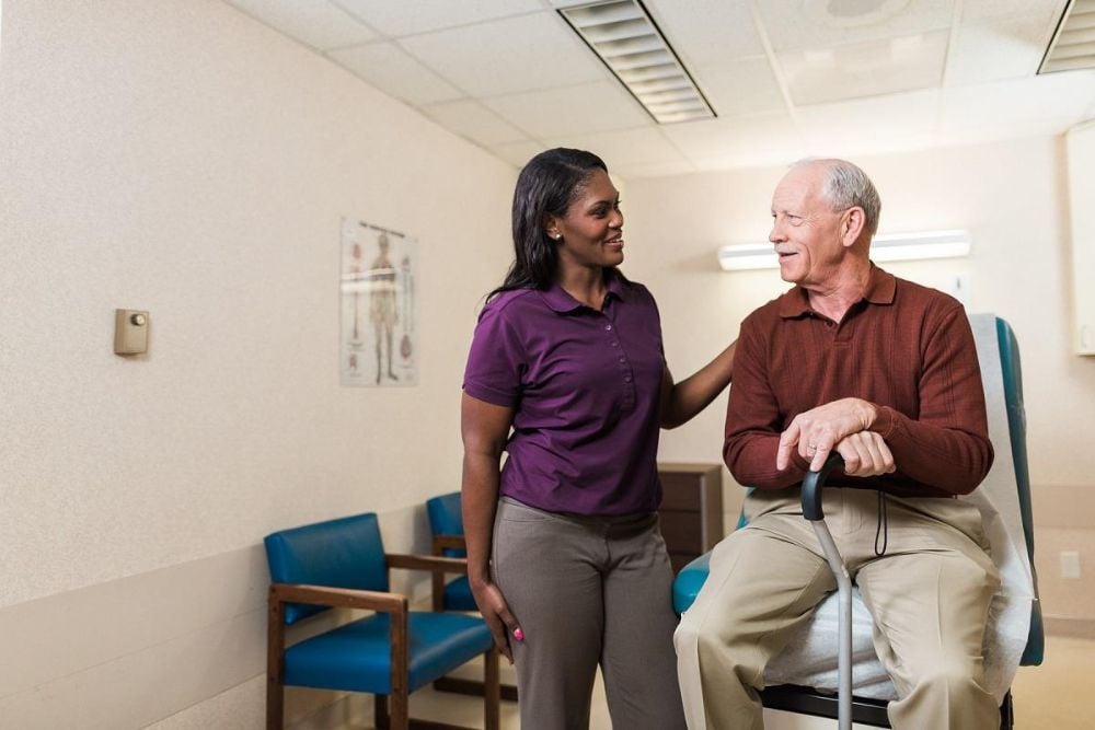 smiling caregiver comforting a senior at doctors office