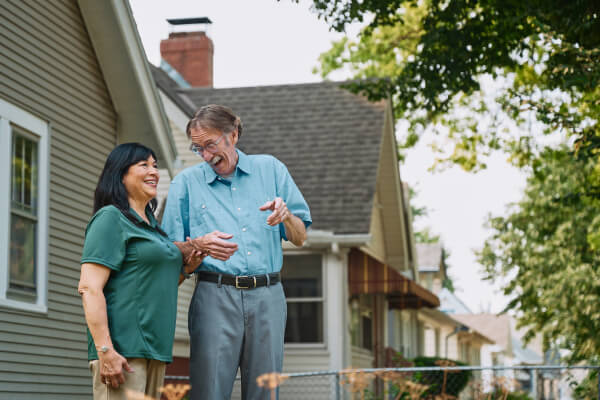 A Home Instead caregiver walks outdoors with an elderly man, both laughing and enjoying the fresh air, representing active engagement and companionship.