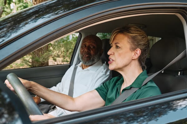 A Home Instead caregiver assists an elderly man in the passenger seat of a car, preparing for a safe and comfortable ride, showcasing reliable transportation support.