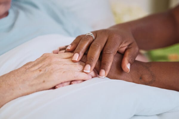 A close-up of a Home Instead caregiver's hands gently holding the hands of an older adult, showcasing compassion, trust, and care.