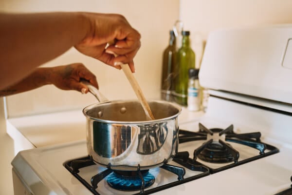 Close-up of hands stirring a pot on a stovetop, symbolizing in-home care services like meal preparation, with a warm, homey feel.