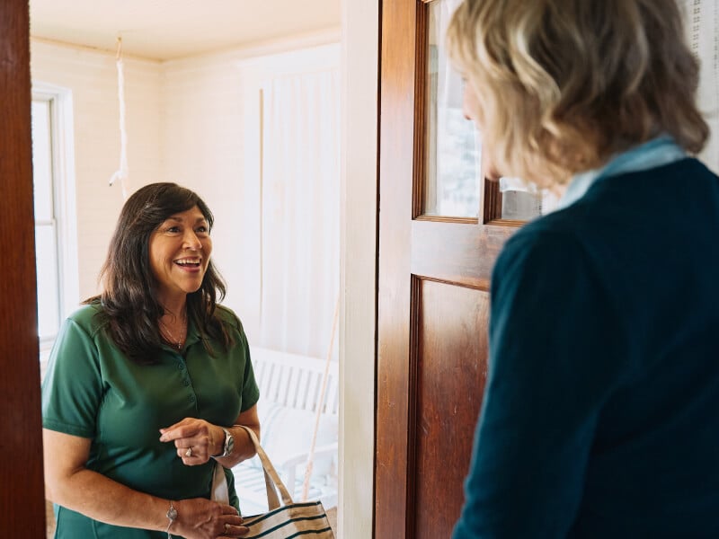 Home Instead Caregiver waters flowers while on back porch with senior client.