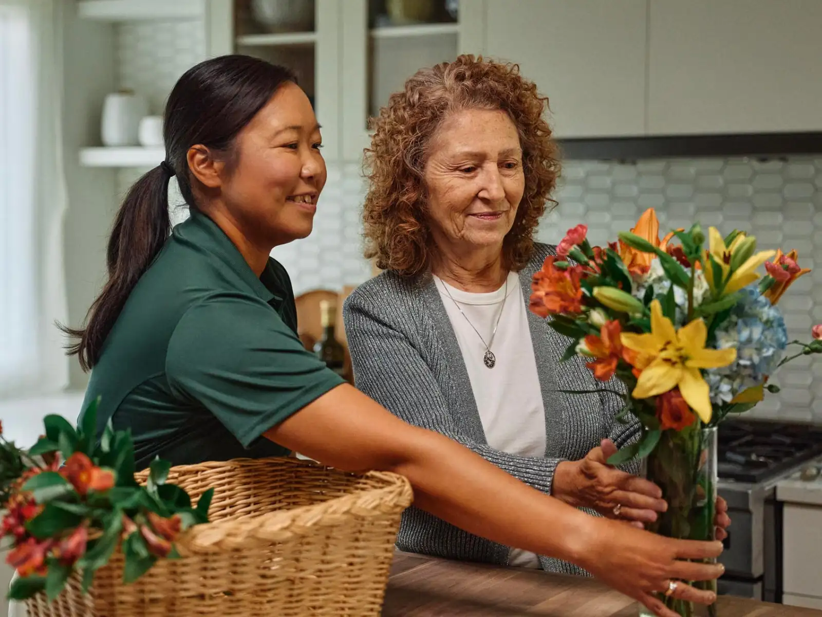 A Home Instead caregiver assists an elderly woman in arranging a bouquet of colorful flowers in a vase, highlighting moments of shared creativity and joy.