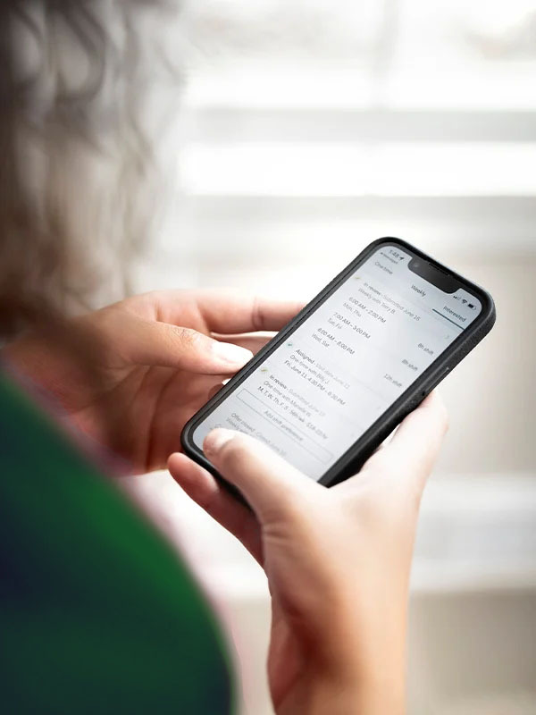 A Home Instead client holds a smartphone displaying a schedule or app interface, highlighting convenient technology for managing appointments and tasks.