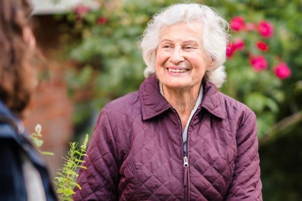 senior woman smiles while sitting outside with younger woman