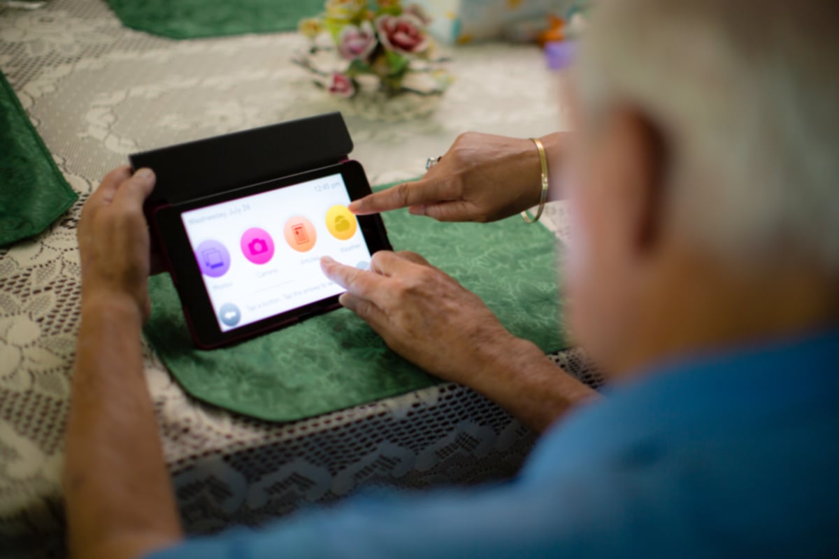 Senior pointng to Home Instead tablet displaying icons and options to enhance his life.