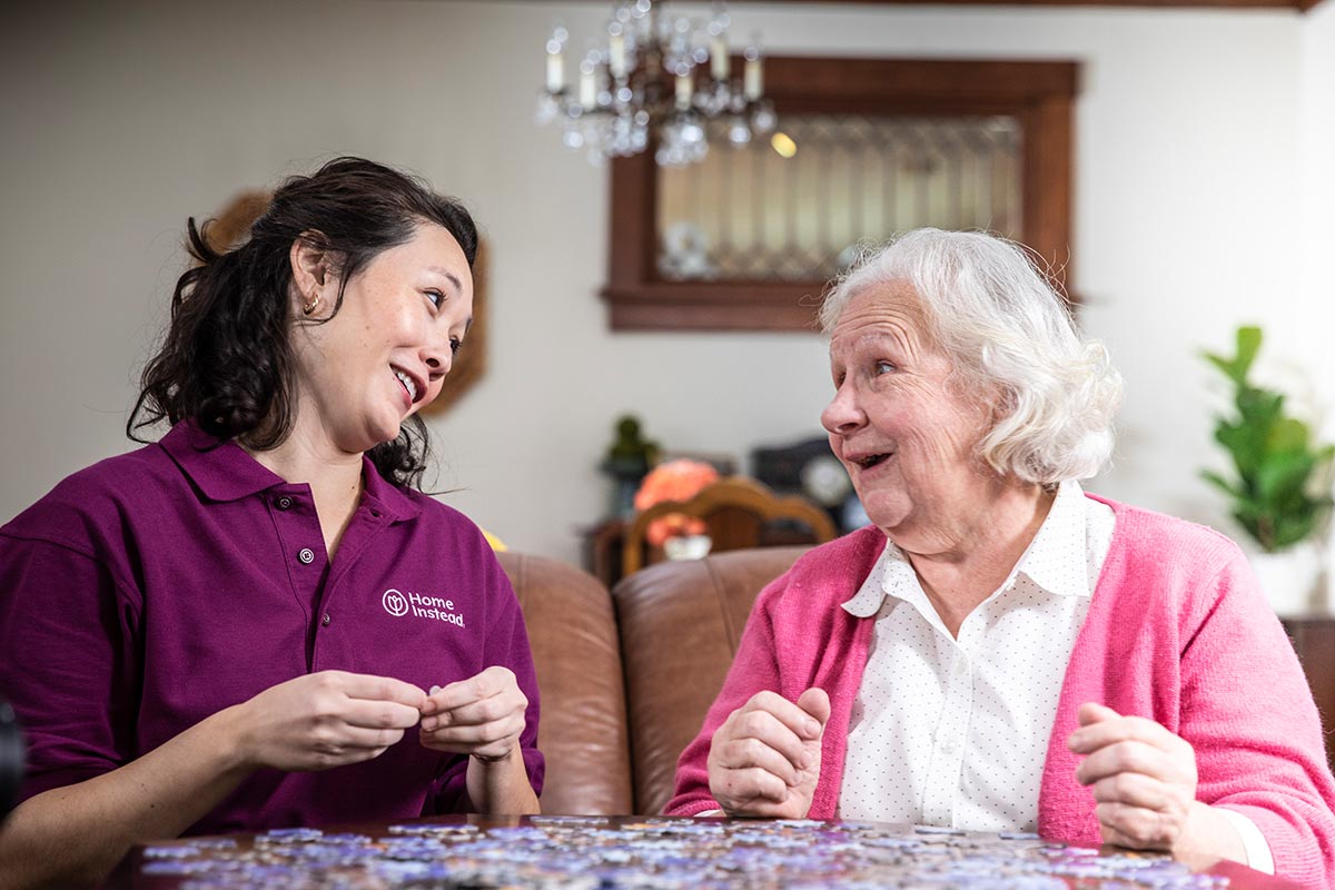 Home Instead CAREGiver and senior smiling and working on puzzle