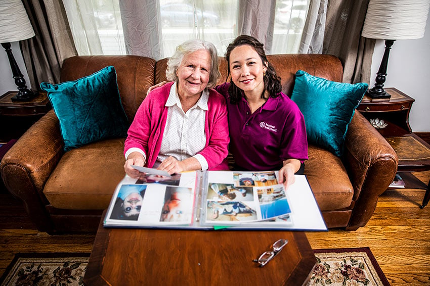 Home Instead CAREGiver and senior smiling looking at photo album