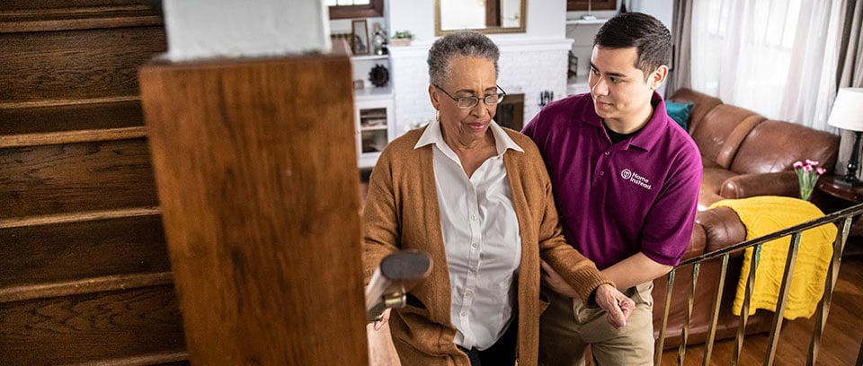 Home Instead Caregiver helps senior woman walking up the stairs at home