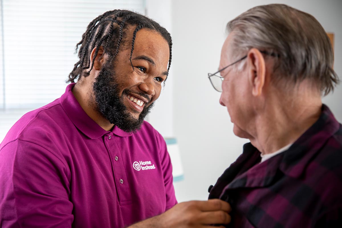 Home Instead Caregiver helps senior man button shirt at home