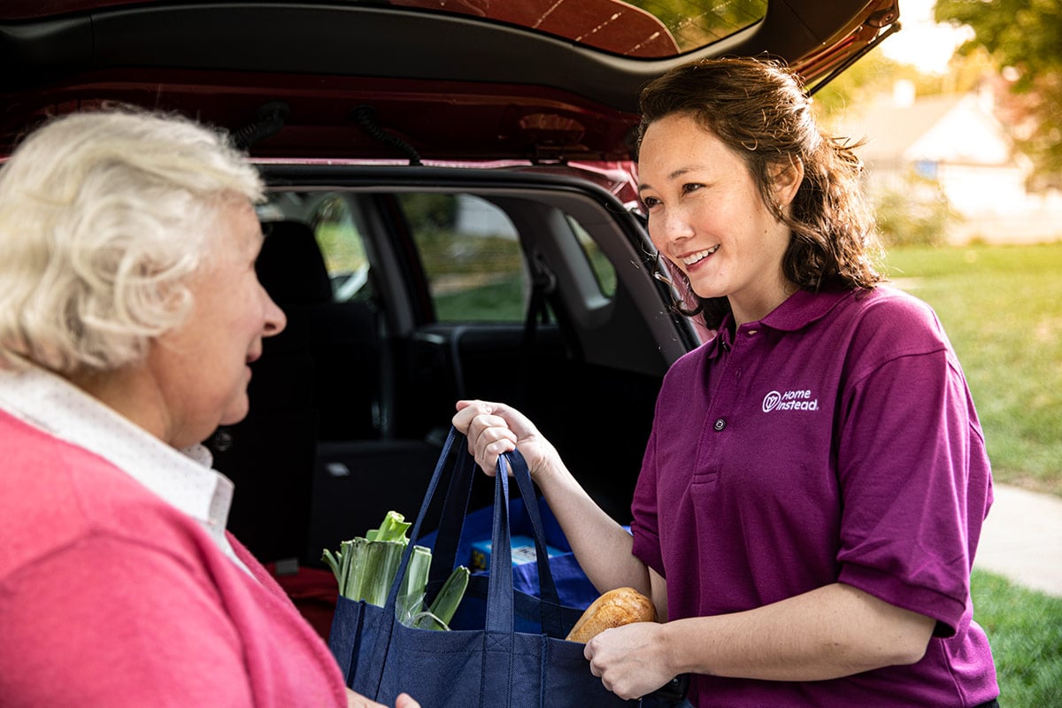 Home Instead Caregiver helps senior woman unload groceries from vehicle