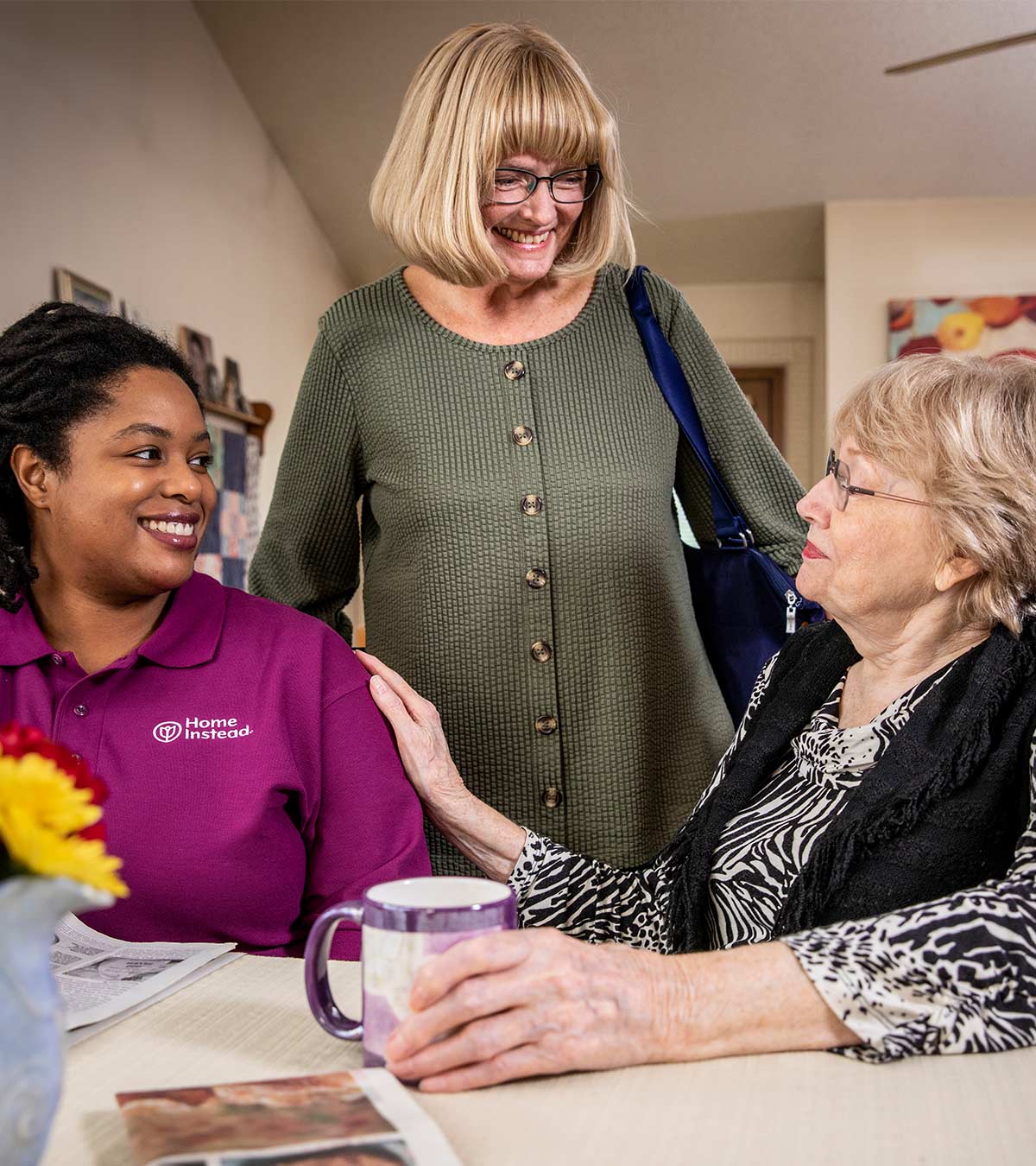 Home Instead Caregiver sits talking with senior and daughter at home