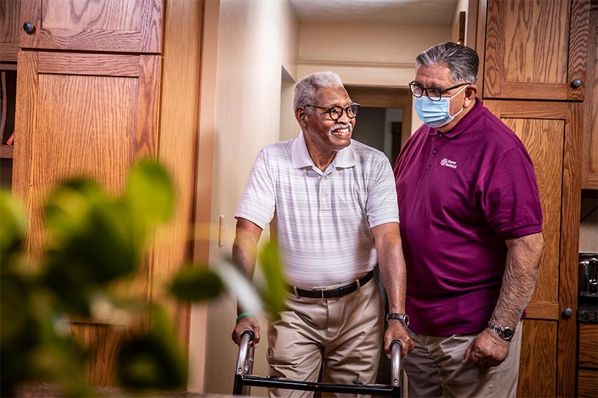 Home Instead Caregiver waters flowers while on back porch with senior client.