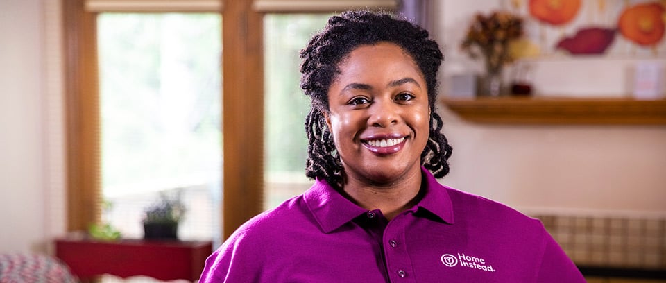 Home Instead Caregiver stands smiling in home living room