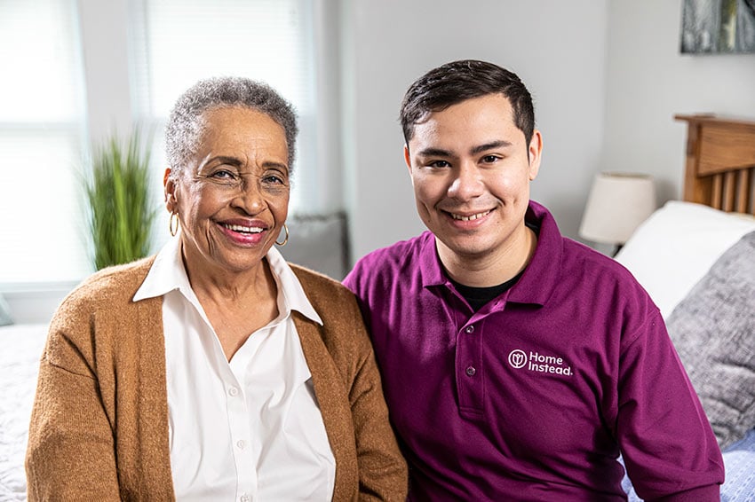 Home Instead Caregiver smiles with senior woman at home in living room.