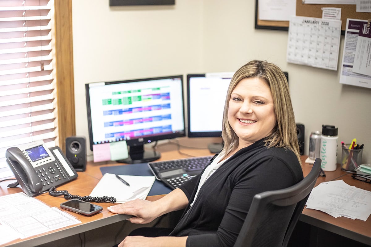 Home Instead care coordinator smiles while sitting in office.